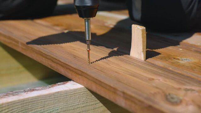 Deck construction, builder hand with electric screwdriver installing impregnated wooden boards