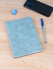 Design concept - top view of notepad with phone, bookmarks, binder and pen on wooden table