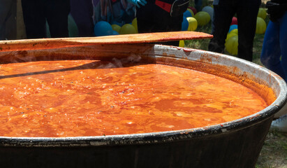Tomato soup with pasta is a dish of Polish cuisine. Hot Zupa pomidorowa in a large cauldron at the field kitchen at a food fair. A popular soup made from grated tomatoes in their own juice. - obrazy, fototapety, plakaty