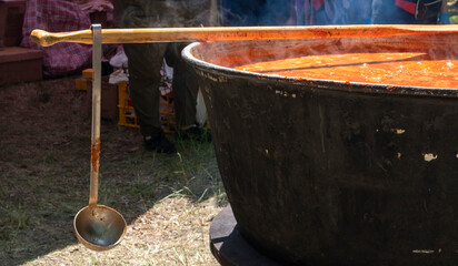 Tomato soup with pasta is a dish of Polish cuisine. Hot Zupa pomidorowa in a large cauldron at the field kitchen at a food fair. A popular soup made from grated tomatoes in their own juice. - obrazy, fototapety, plakaty