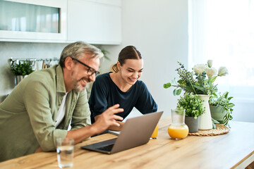 Obraz premium Happy father and daughter using a laptop, leaning on a kitchen island.