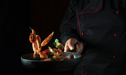 Cooking shrimp in the restaurant kitchen. Flight of prawn over a frying pan in the cook's hand. Black space for recipe or menu - obrazy, fototapety, plakaty