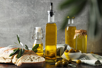 Bottles of olive oil, olives and slices of bread on gray background