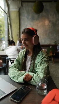 The Young Girl In Headphones Is Communicating Virtually Via Her Laptop While Dining In The Restaurant.