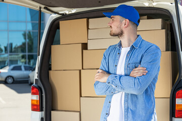 Obraz premium A courier with a tablet in his hands near a car with boxes