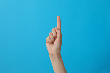 Female hand showing one finger on blue background - obrazy, fototapety, plakaty