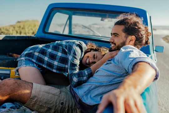 Young couple sitting in the back of a truck on a road trip on the beach