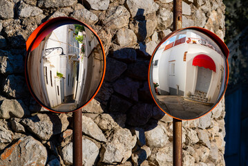 Two circular old traffic mirrors with red frames reflecting narrow streets in a village on Capri island, Italy. Holiday atmosphere on a sunny summer day in mediterranean surrounding.