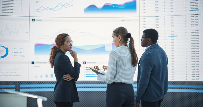 Diverse Team Of Data Scientists Analyzing Information And Graphs On Big Led Wall In Modern Monitoring Office. Multiethnic Colleagues Discussing Financial Strategies, Risk Factors, Potential Deals. - Powered by Adobe