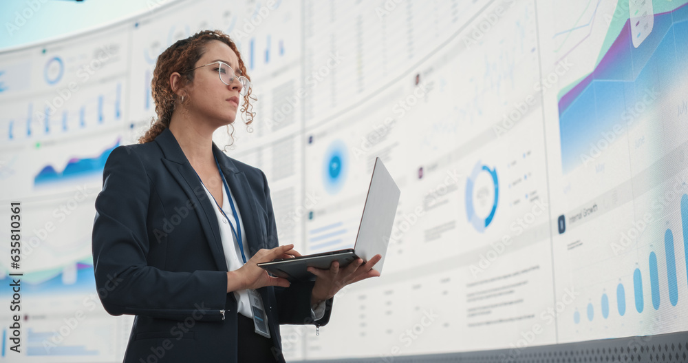 Poster successful hispanic businesswoman holding laptop computer and reviewing financial reports on digital