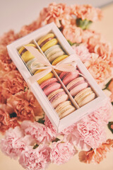 Dessert French Macarons in present box on a background of flowers. Sweet dessert on a flowers background. Still life with macaroni cakes and different flower. Delivery concept, coffee and flower shop