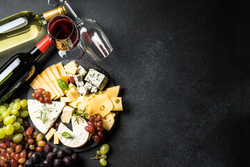 Cheese platter and wine. Craft cheese set, fresh grape, wine bottles on cutting board. Top view at black background.