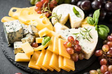 Cheese platter with craft cheese assortment and grape on slate board.
