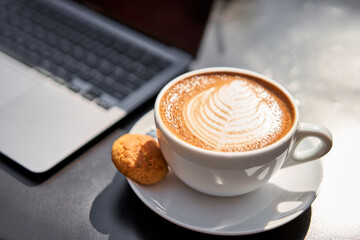 A man drinks coffee, holds a cup of hot Peanut latte in his hand. The table in the coworking space of the coffee shop. A cup of coffee on the veranda on a sunny day. Coffee break at the cafe. Close-up