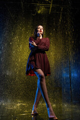 Lady in classic dress with long sleeves changes position of hands. Stream of rain falls rapidly and breaks on glossy dark surface in night light