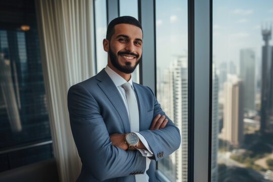 Young handsome Emirati business man in UAE traditional outfit standing on office with crossed arms. Arabic ambitious mature businessman.