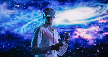Young Male Wearing a Virtual Reality Headset and Using Controllers in a Futuristic Room with...