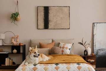 Cozy composition of bedroom interior with mock up poster frame, bed, orange bedding, corgi dog, wooden bedside table, black rack, stylish lamp, sculpture and personal accessories. Home decor. Template