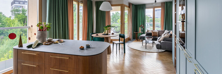 Interior design of colorful apartment with wooden kitchen island, round table, chairs, sofa, pillows, green curtain, carpet, hanging lamp, panels floor and personal accessories. Home decor. Template.