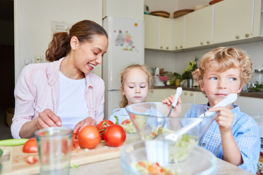 Happy mother with children preparing salad in kitchen