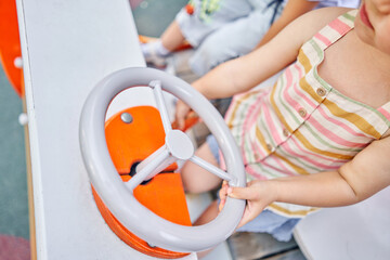 Little girl playing, she is a car driver holding steering wheel on playground. A sunny summer evening, a fun childhood.