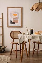 The stylish dining room with round table, rattan chair, lamp, poster and kitchen accessories. Beige...