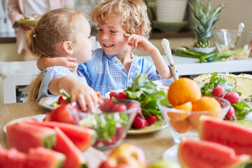 Happy siblings near table with fruits and vegetables at home