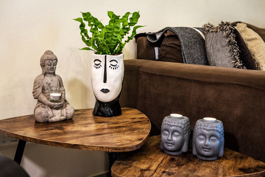 Interior details. Head-shaped candle holders, flower pot with bloom, and Buddha tealight statue on small tables. Selective focus.