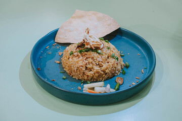 Selective shot of a plate of Nasi Goreng or Fried Rice with cracker, carrots, and cucumber on isolated sage green pastel background