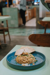 Portrait or vertical and selective focus shot of a plate of Nasi Goreng or Fried Rice with cracker, carrots, and cucumber on isolated sage green pastel background