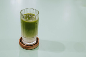 Selective focus shot of a glass of Ice Matcha or Japanese Green Tea Latte on wooden coaster on isolated sage green pastel table