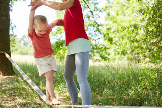 Playful girl slacklining with mother in garden