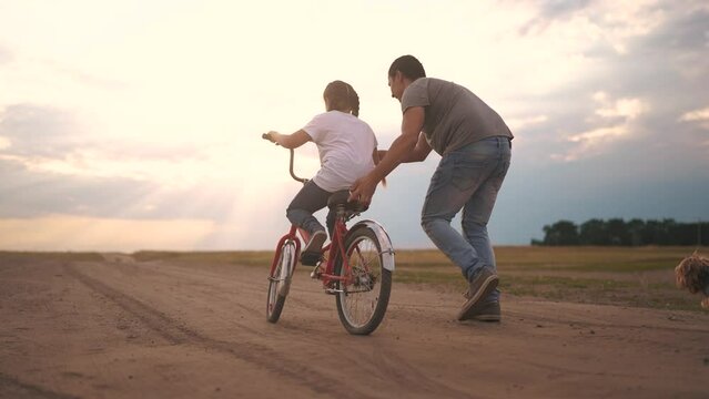dad teaches son to ride a bike. happy family kid dream concept. the boy sat on bicycle for the first time, his father teaches boy to ride a bicycle. lifestyle dog runs with family, fun family pastime