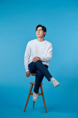Beautiful asian successful man sitting at white chair and posing to the camera. Copy space.