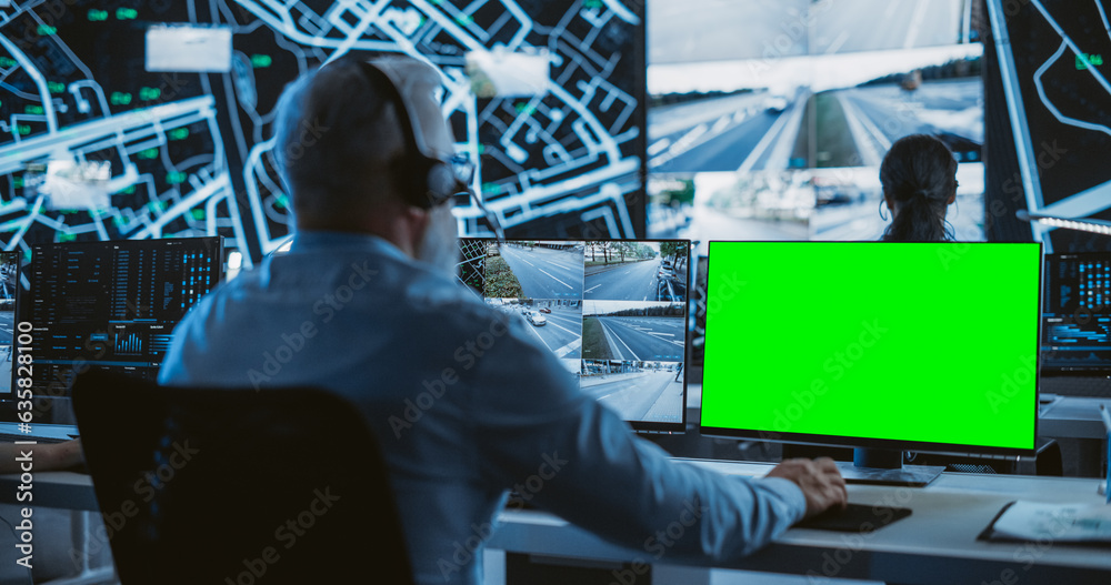 Poster Technical Support Manager Using Headphones and a Computer with Green Screen Mock Up Display. Specialist in a Dark High-Tech Monitoring Room, Concentrated on a Call and Computer Work