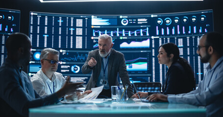 Senior Team Leader is Making a Presentation on a Management Meeting in a Big Data Monitoring Company. Diverse Team of Data Scientists Discussing Graphs and Reports on Big Digital Screen in the Office