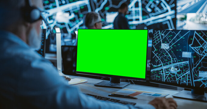 Middle Aged Surveillance Specialist Working on a Computer with Green Screen Mock Up Display. Manager Effectively Multitasking with Supporting Clients on a Phone Call and Computer Work