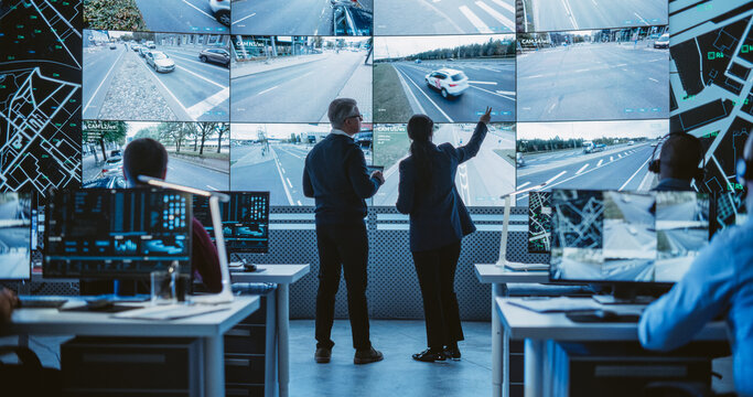 Two Diverse Male and Female Software Engineers Discuss Live Analysis Feed with City Road and Traffic Updates. Managers and Data Scientists Collaborate in a Modern Monitoring Office
