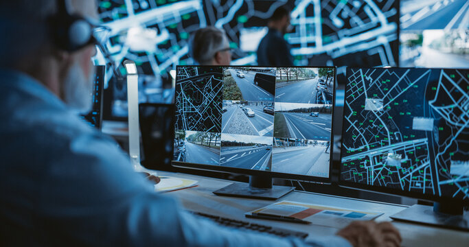 Technical Customer Support Specialist is Talking on a Headset while Working on a Computer in a Call Center Control Room Filled Display Screens with Monitoring Software. Over the Shoulder Footage