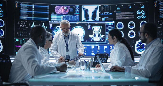 Chief Doctor Conducting a Pre-Operative Assessment Meeting With His Surgical Team. Group of Brain Surgeons Discussing Possible Treatment in an Advanced Laboratory with Interactive Digital Screens