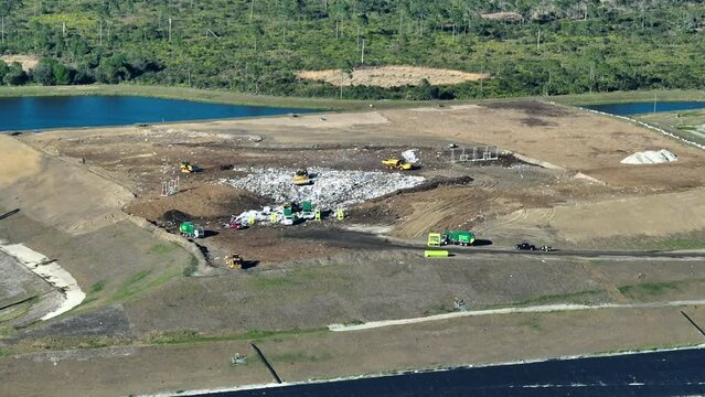 Garbage landfill site with bulldozer tractors burying large amount of trash under the ground. Harmful impact of open waste managment on environment
