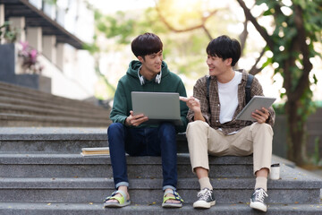 Portrait of two asian man students using tablet and laptop sitting in a university.