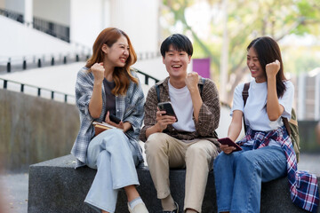 Group of Asian students rejoice with their arms raised in joy after receiving the results of their university entrance exams via their mobile phones.