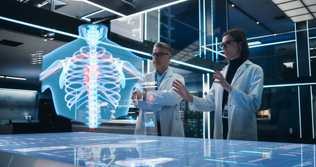 Two Bioengineers Working With Computer-Powered VFX Hologram Of Human Chest With Heart And Blood Flow In Futuristic Lab. Caucasian Man And Woman Working On Innovative Heart Attack Prevention Solution.