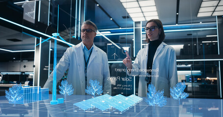 Male And Female Renewable Energy Engineers Using Futuristic Hologram of Wind Turbine Prototype In Computer Powered Laboratory. Caucasian Colleagues Controlling VFX Projection With Gestures.