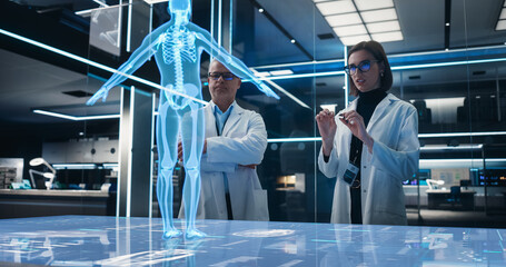 Two Bioengineers Working With Computer-Powered VFX Hologram Of Human Body In Futuristic Lab. Man...