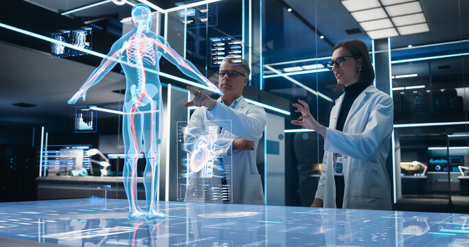 Two Bioengineers Working With Computer-Powered VFX Hologram Of Human Body And Organs In Futuristic Lab. Man And Woman Researching Blood Flow, Developing Innovative Healthcare Solutions.