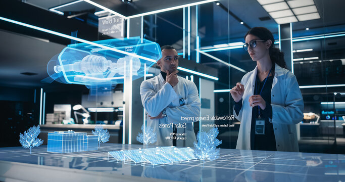 Male And Female Industrial Engineers Using Futuristic Technology Of Hologram of Wind Turbine Prototype In Computer Powered Laboratory. Multiethnic Colleagues Looking At High-Tech VFX Projection.