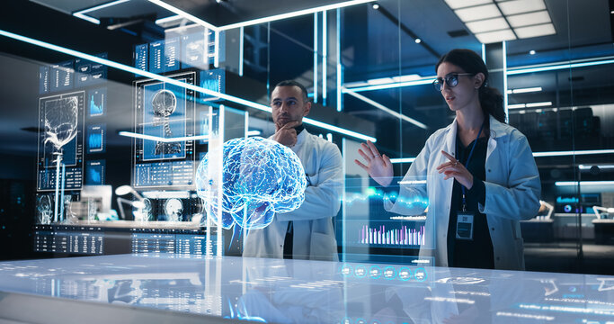 Two Neuroscientists Working With Computer-Powered VFX Hologram Of Human Brain And Nervous System In Futuristic Laboratory. Multiethnic Man And Woman Working On Technological Solutions for Brain Tumor.