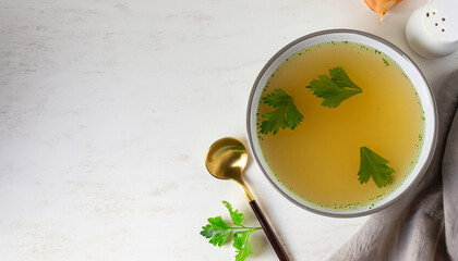 Chicken broth with parsley in bowl on white table. Copy space. Top view. Space for text.